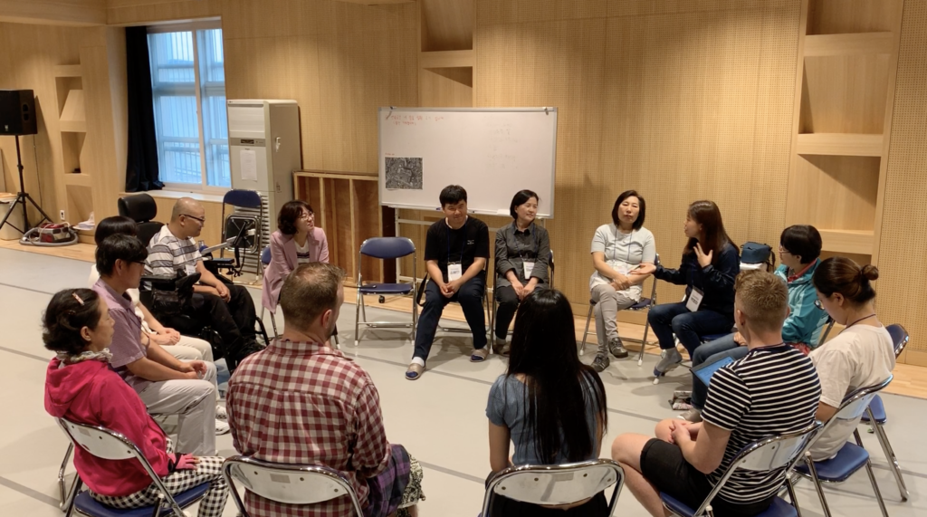 A group of people sitting in a circle in a rehearsal studio