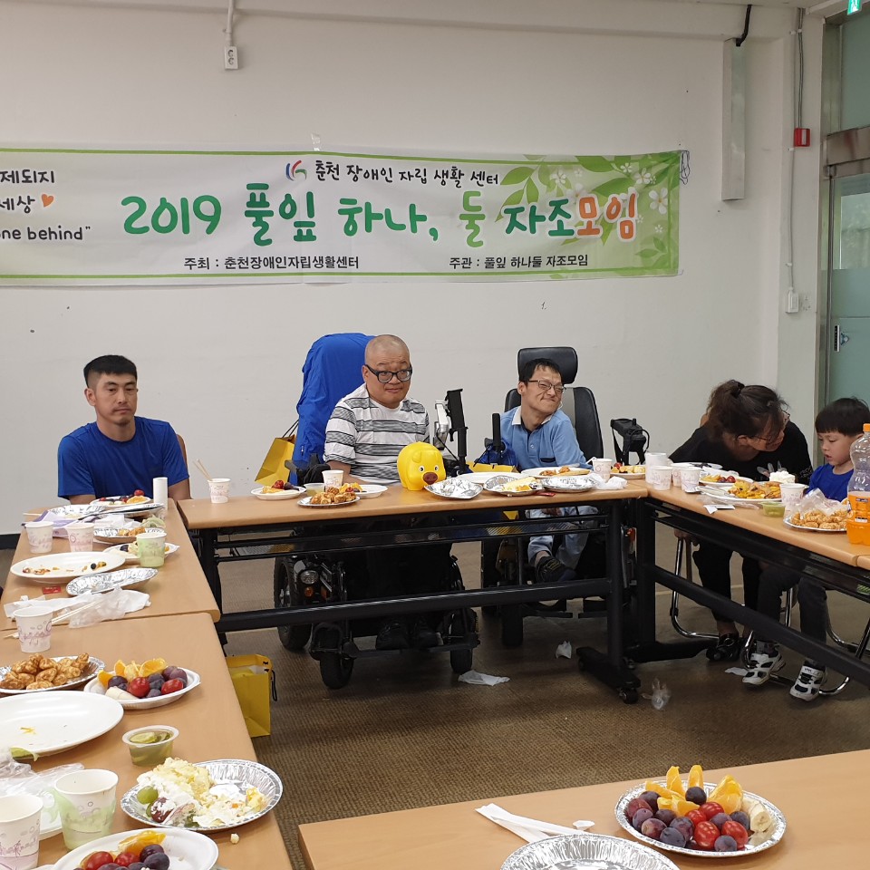 Puliphana and others sitting at a table of food in front of a banner with Korean text