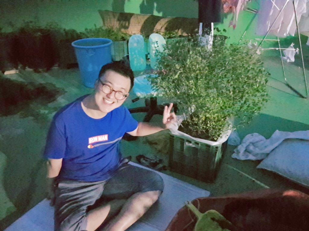 Smiling Sangjun sitting next to a pot plant 