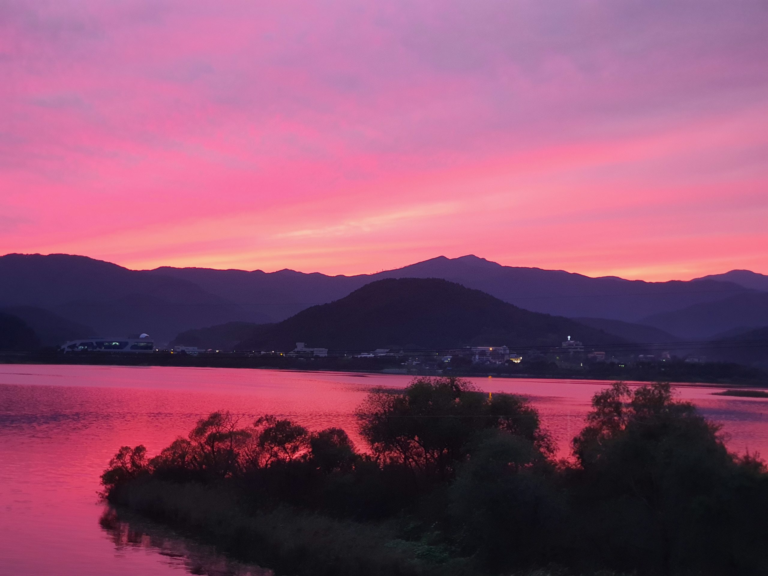 Bright pink sunset over mountains, reflected on lake