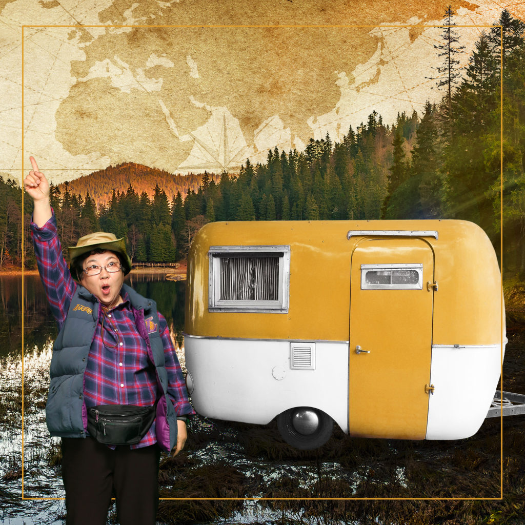 Jeongsun standing next to a vintage caravan, pointing to the sky, with ranges of pine trees in the distance