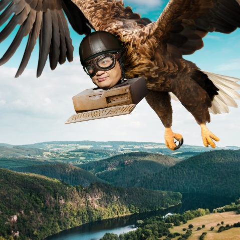 Puliphana's face attached to computer parts and the body of an eagle, flying high above a river in the countryside